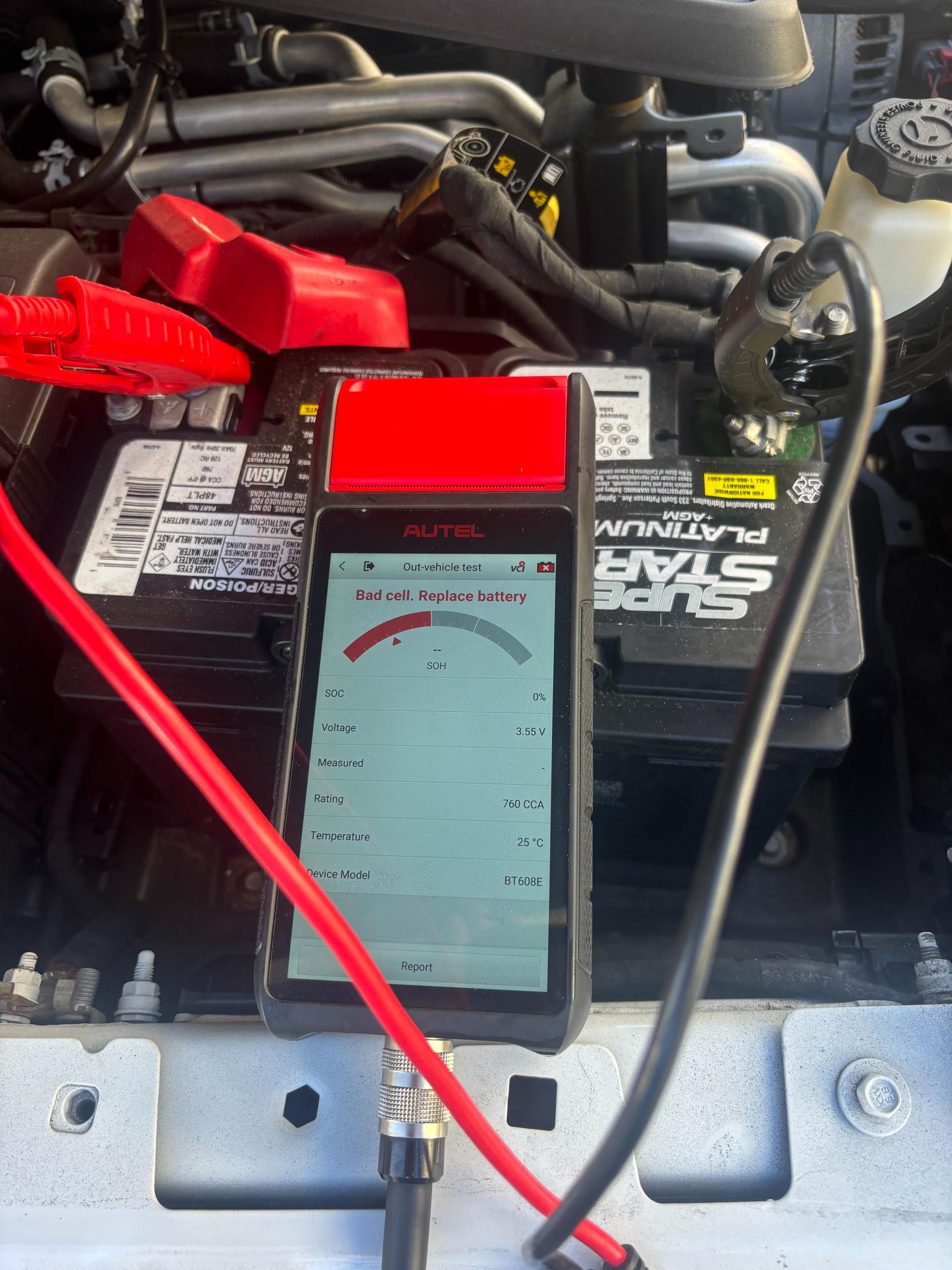A battery tester connected to a car battery. Red and black cables attached, reading displayed on the device.