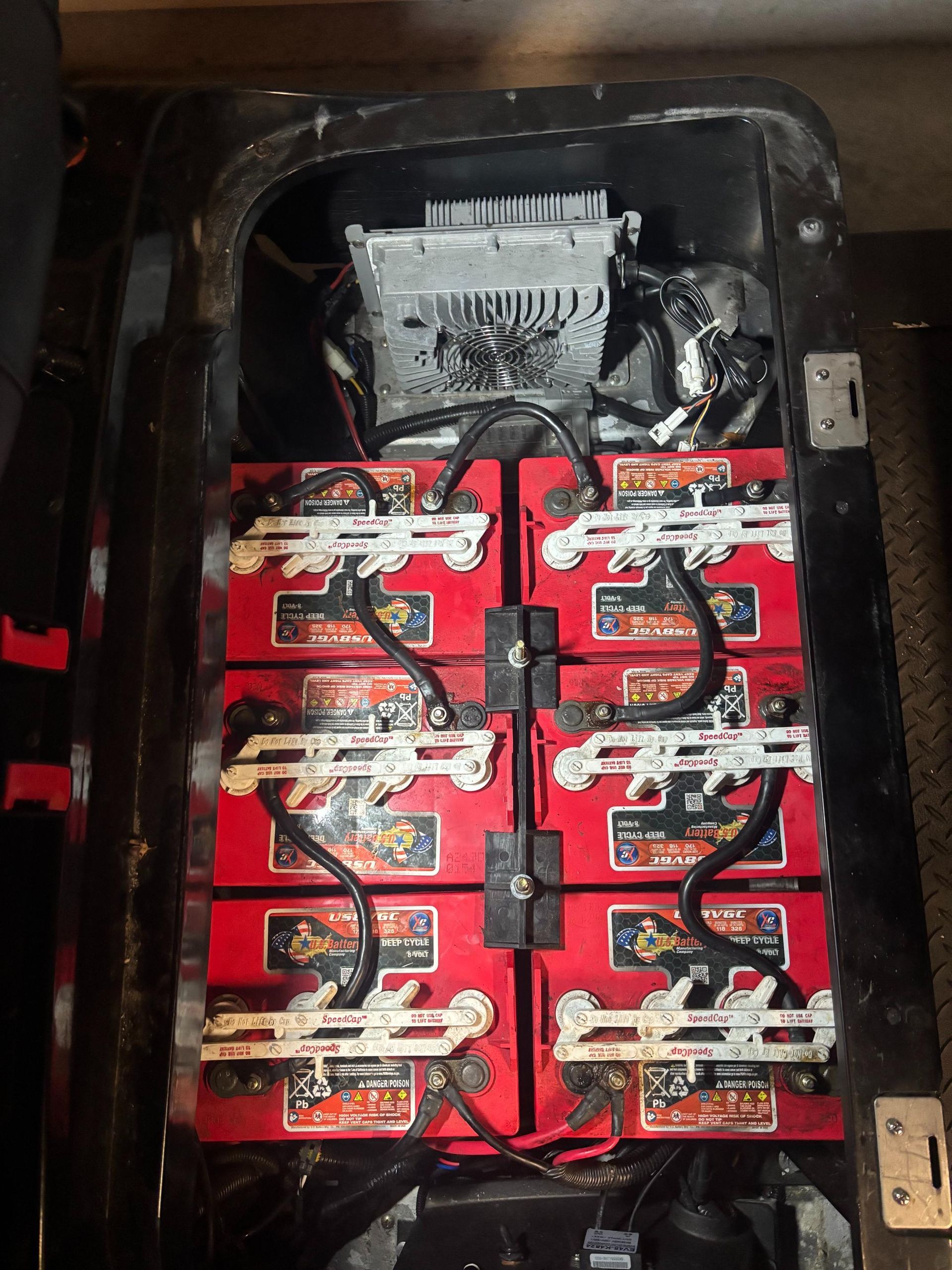 Eight red batteries wired in a golf cart battery compartment with a charger on top.