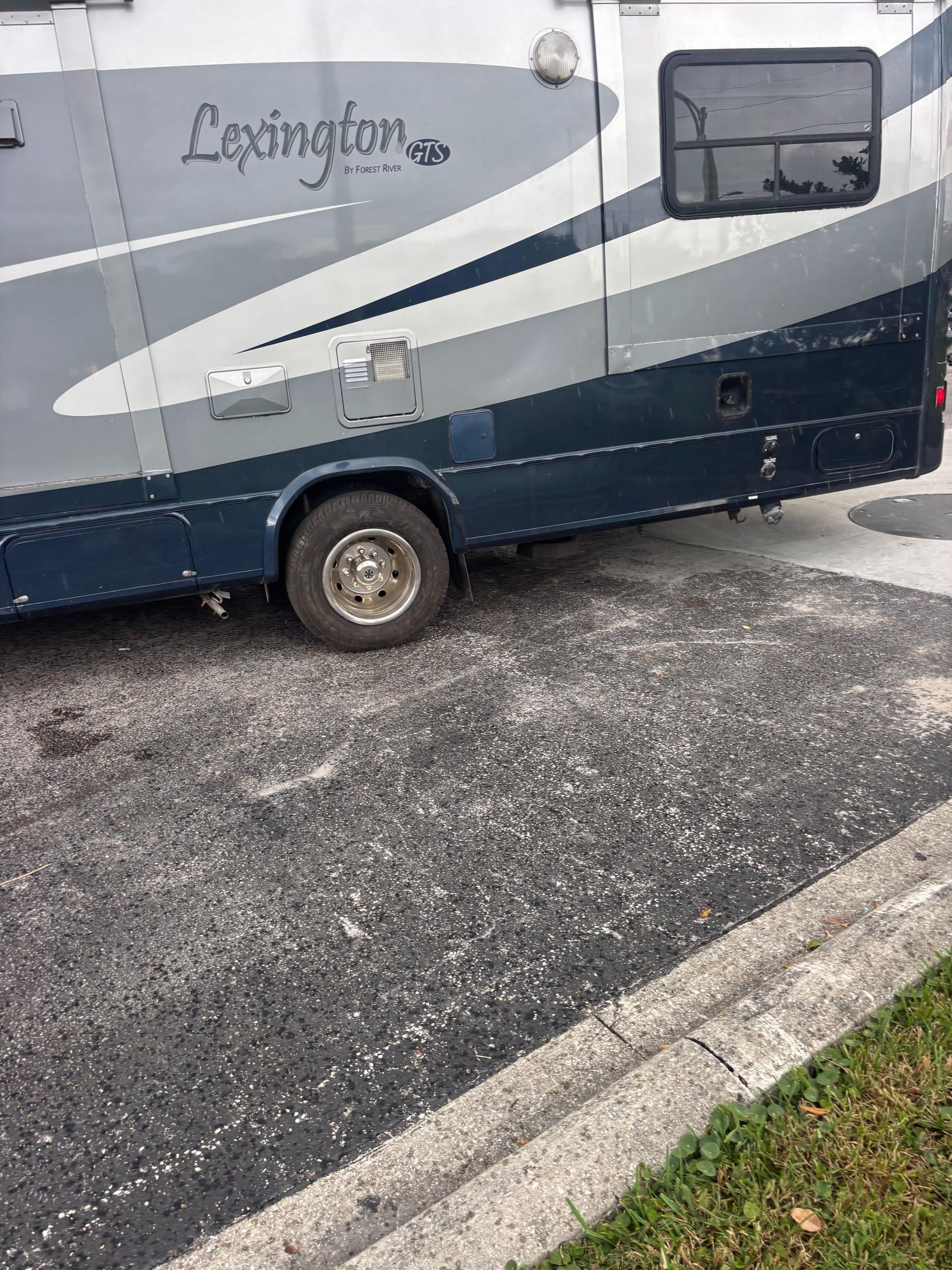 Side view of a blue and gray Lexington RV parked on a black surface with debris.