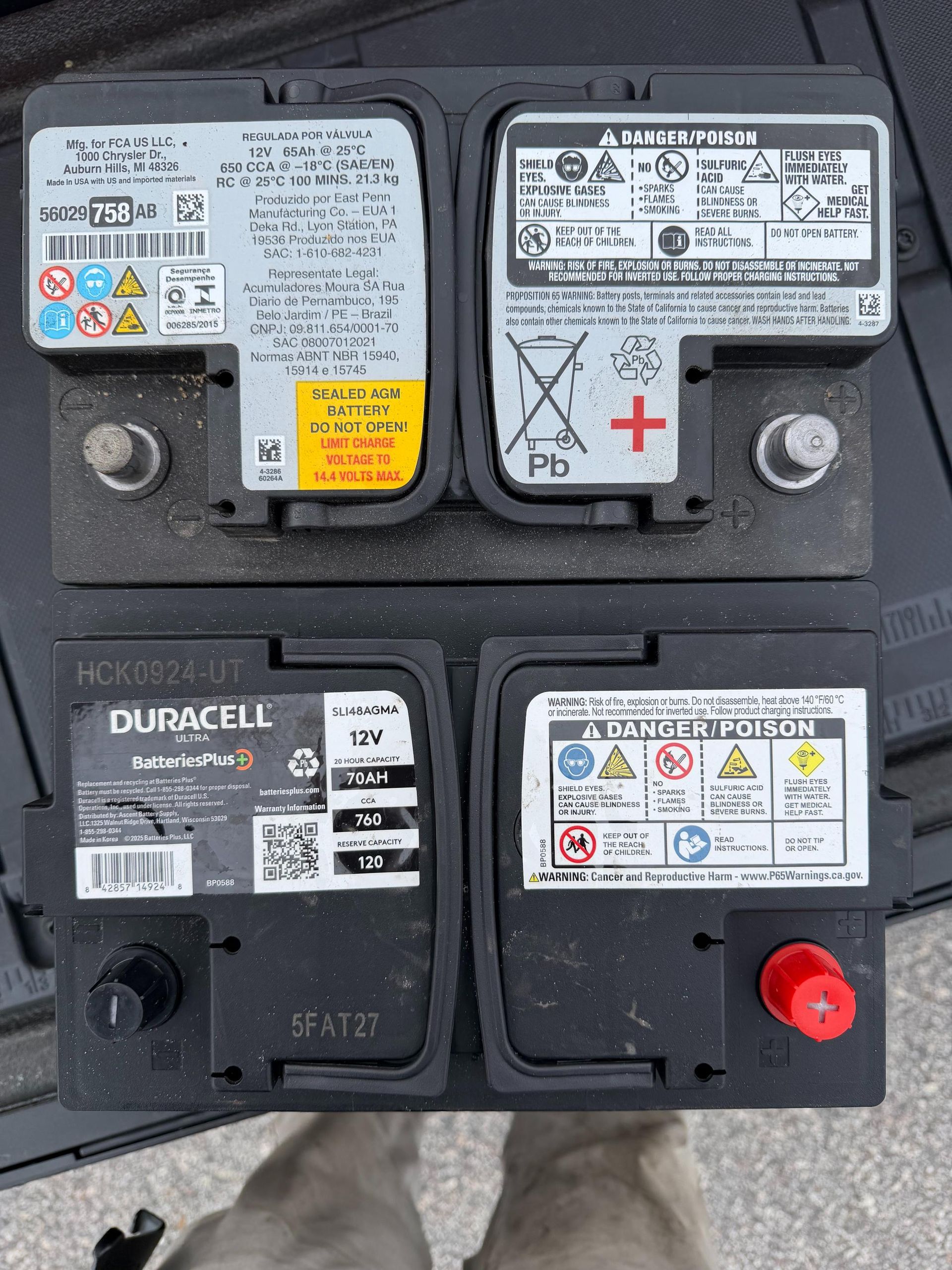 Two car batteries, one top, one bottom, side by side. Black, with labels and terminals.