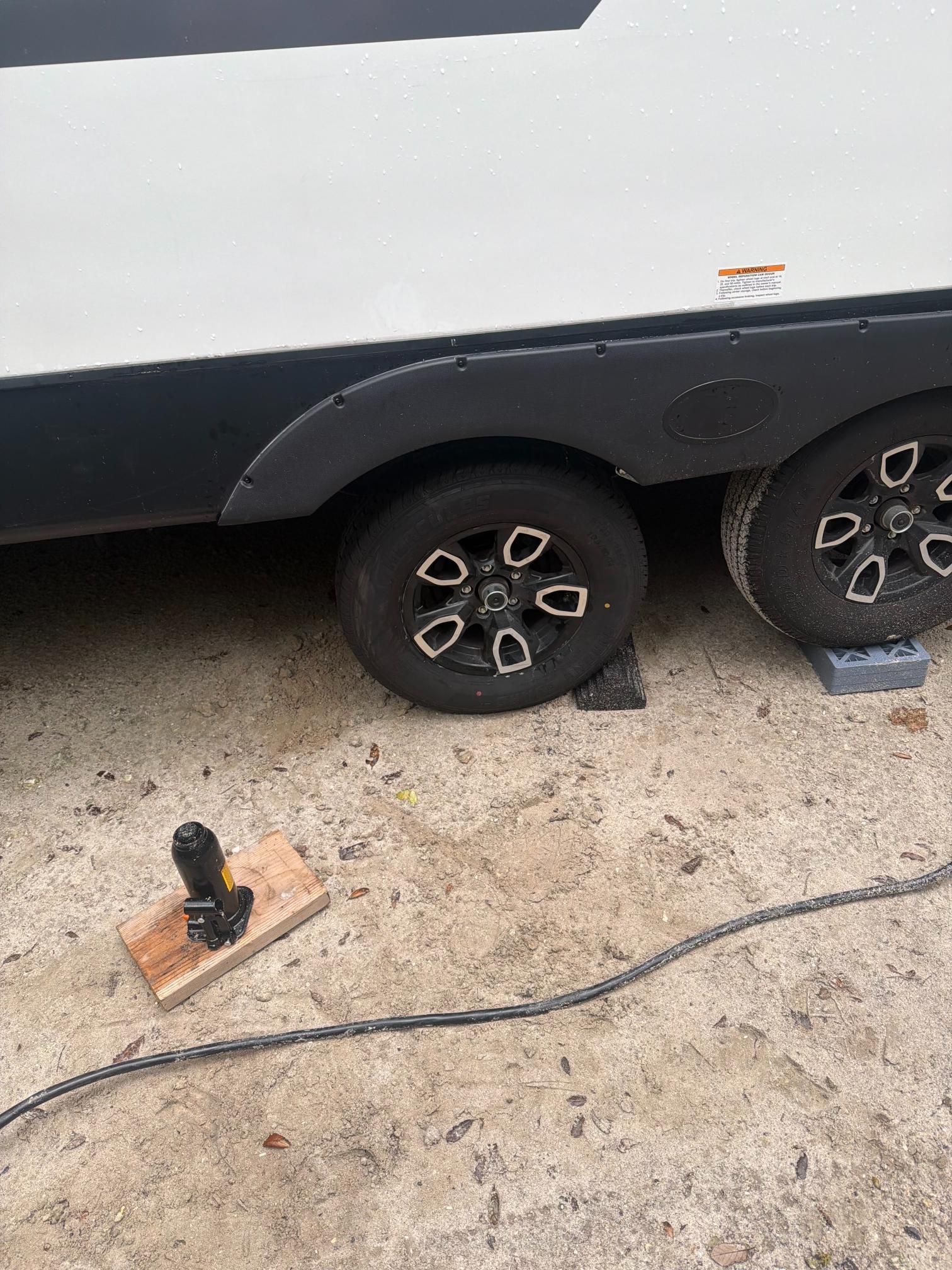Black RV tires on blocks, black wheels with white accents. Power cord and a block with a jack nearby.