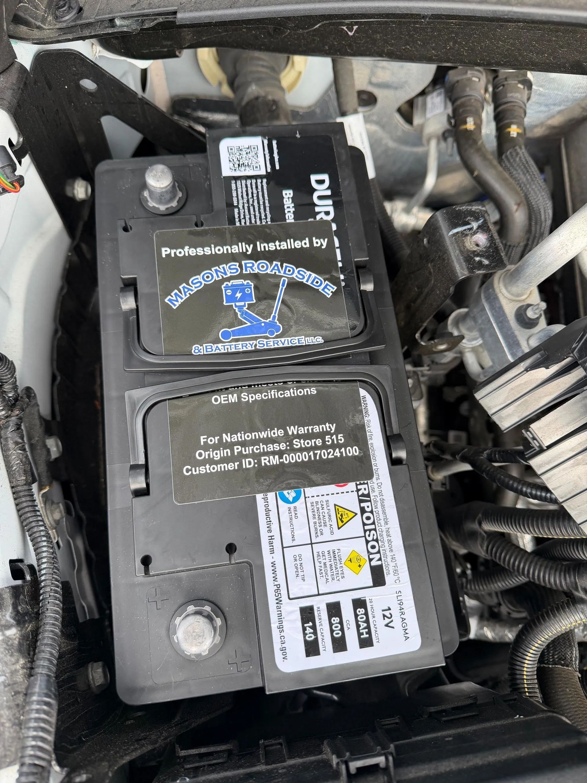 Car battery in engine compartment with warning labels.