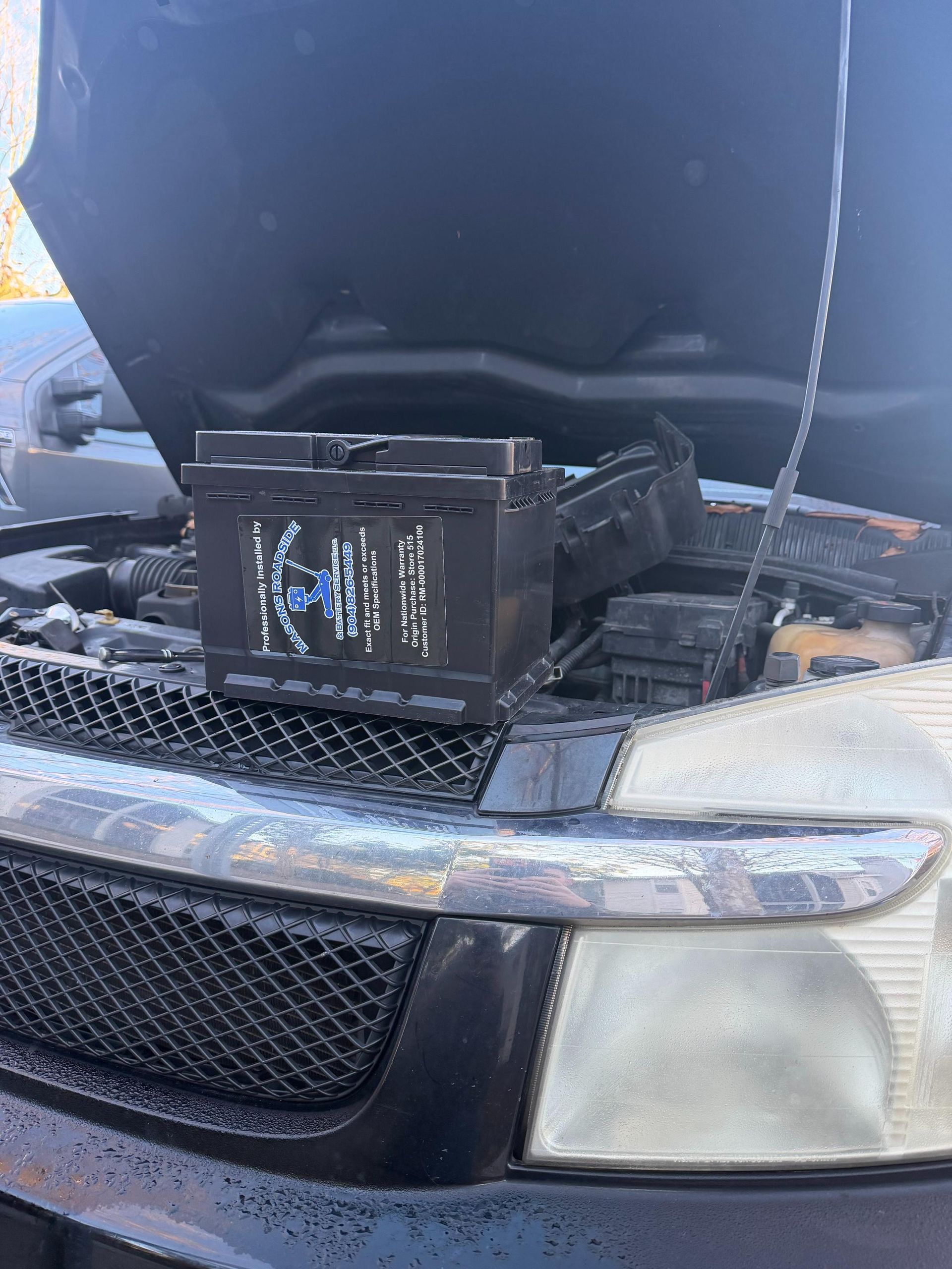 Black car battery sitting on a car engine bay, hood open.