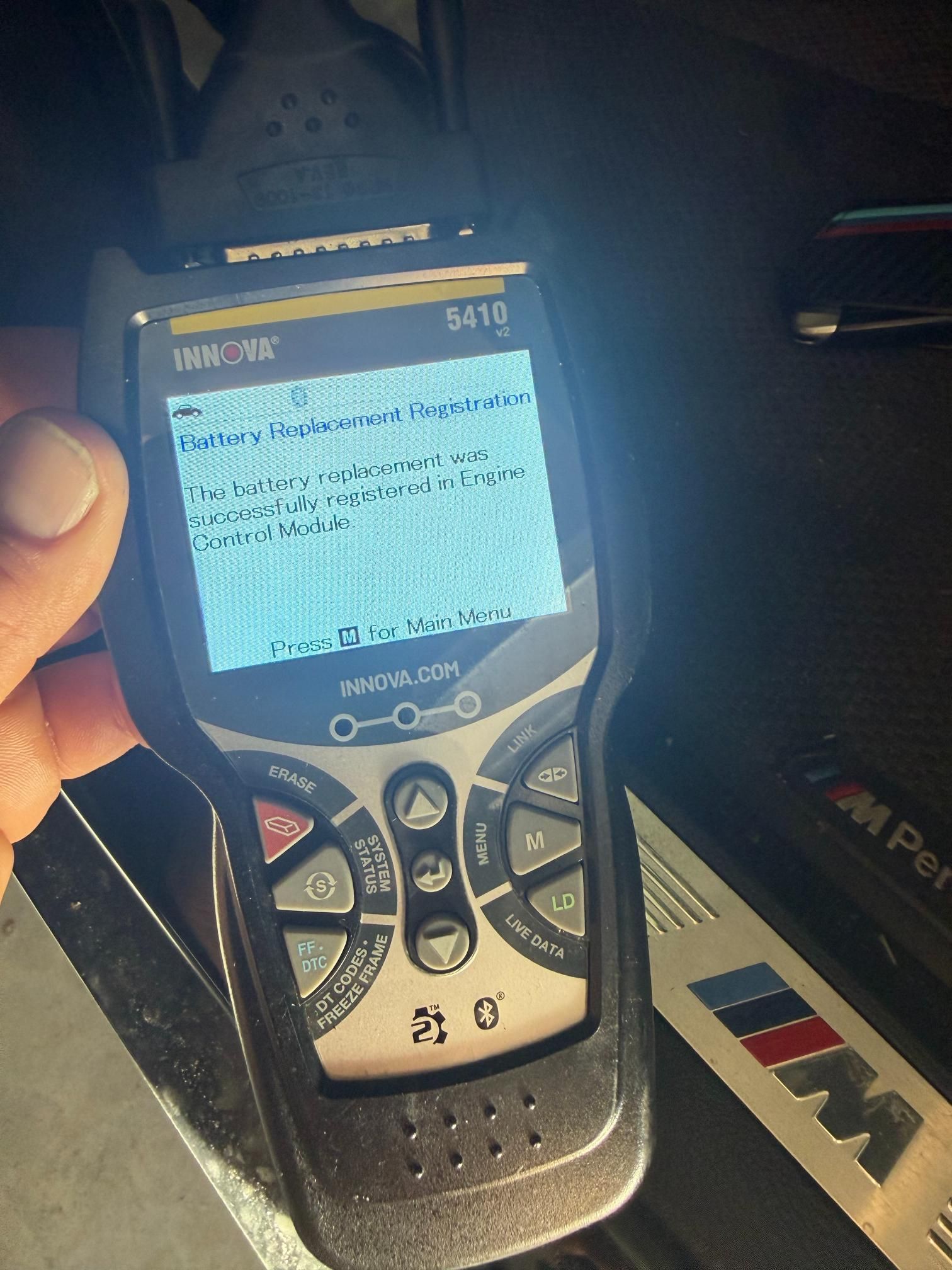 Hand holding an automotive diagnostic tool displaying text related to a car's battery and system.