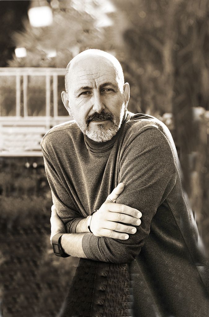 A woman is sitting at a desk with a laptop and a vase of flowers.