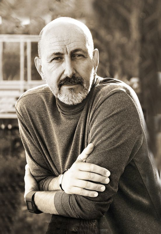 Person working at a wooden desk with a laptop, a plant, and a vase of greenery.