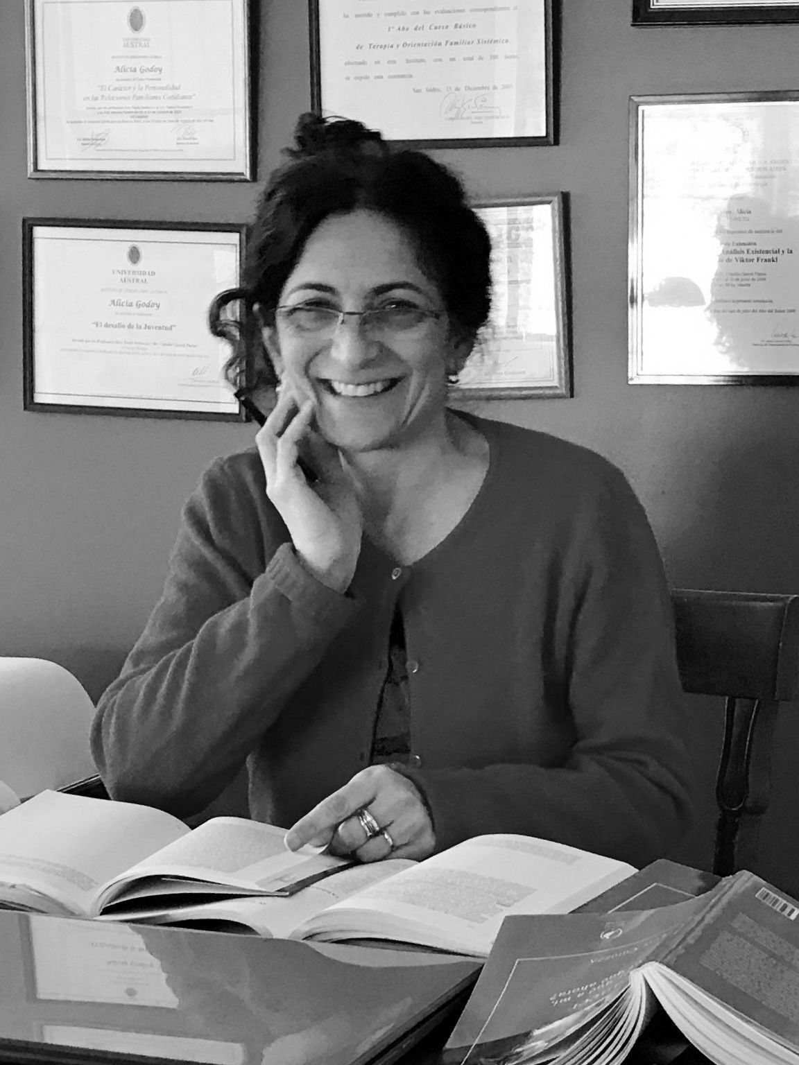 Una mujer está sentada en un escritorio leyendo un libro y sonriendo.