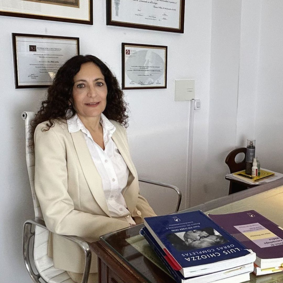 Una mujer está sentada en un escritorio con una pila de libros encima.