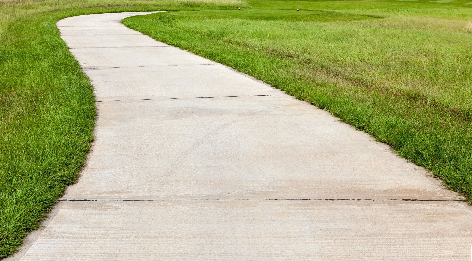 A concrete walkway going through a grassy field