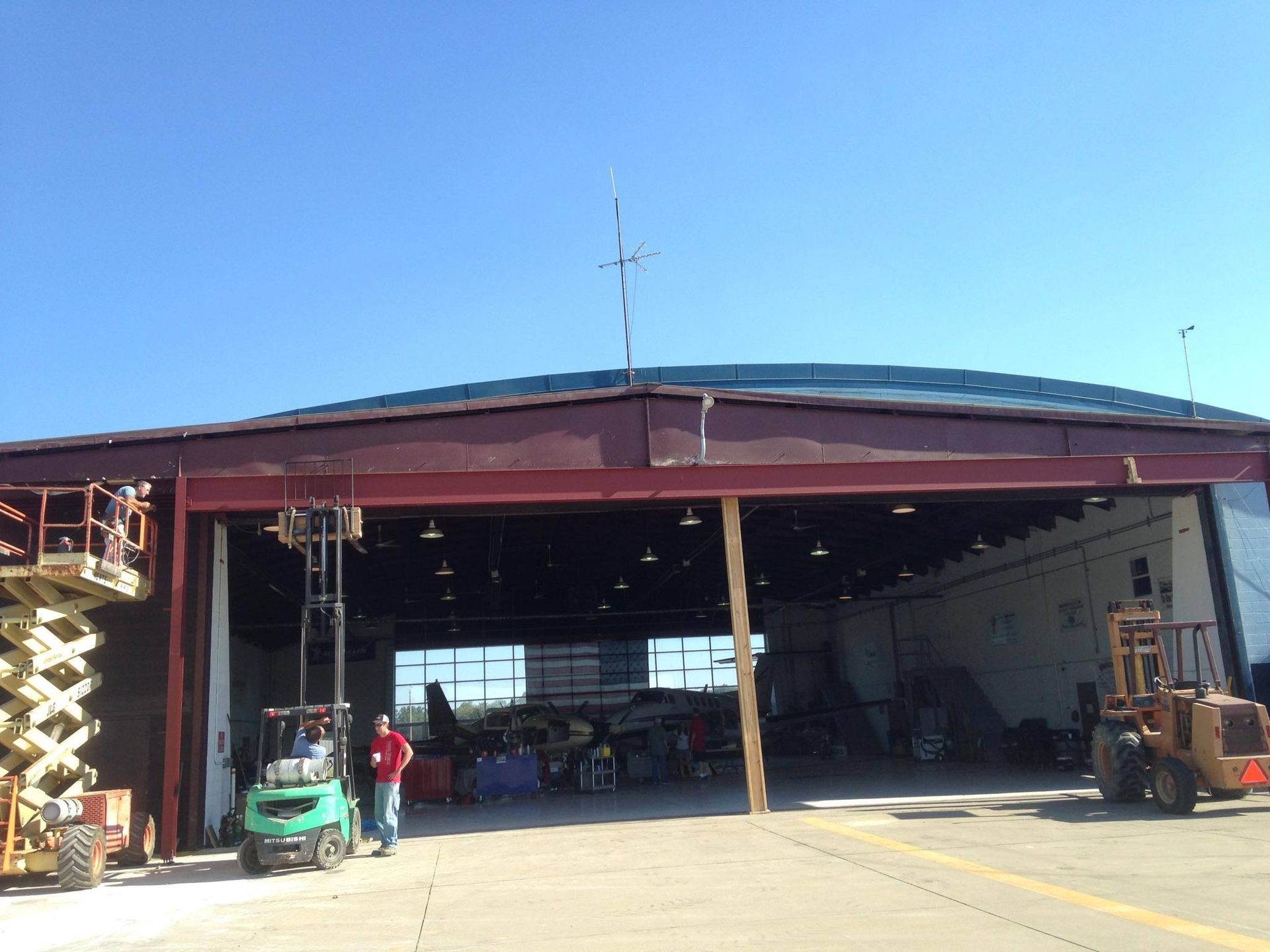 A man is standing in front of a large building with a forklift in front of it