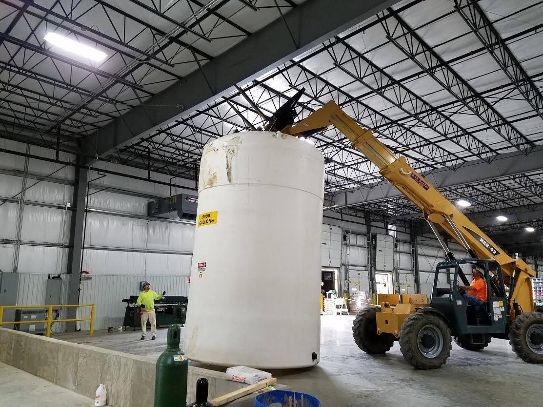 A large white tank is being lifted by a crane in a warehouse