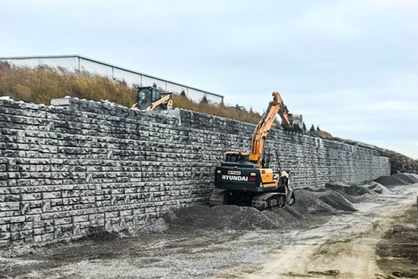 A large excavator is working on a stone wall.