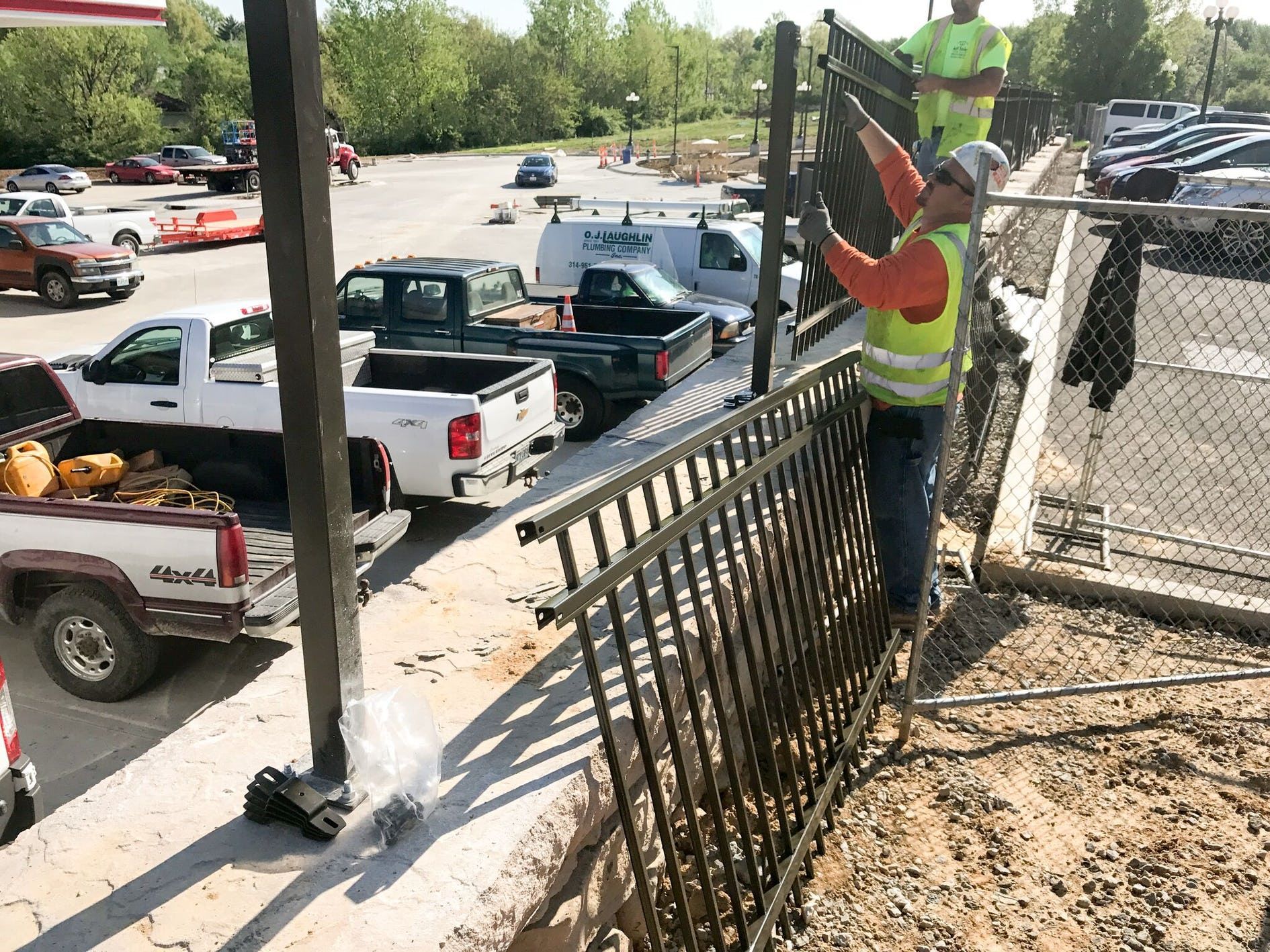 A man is working on a chain link fence in a parking lot.