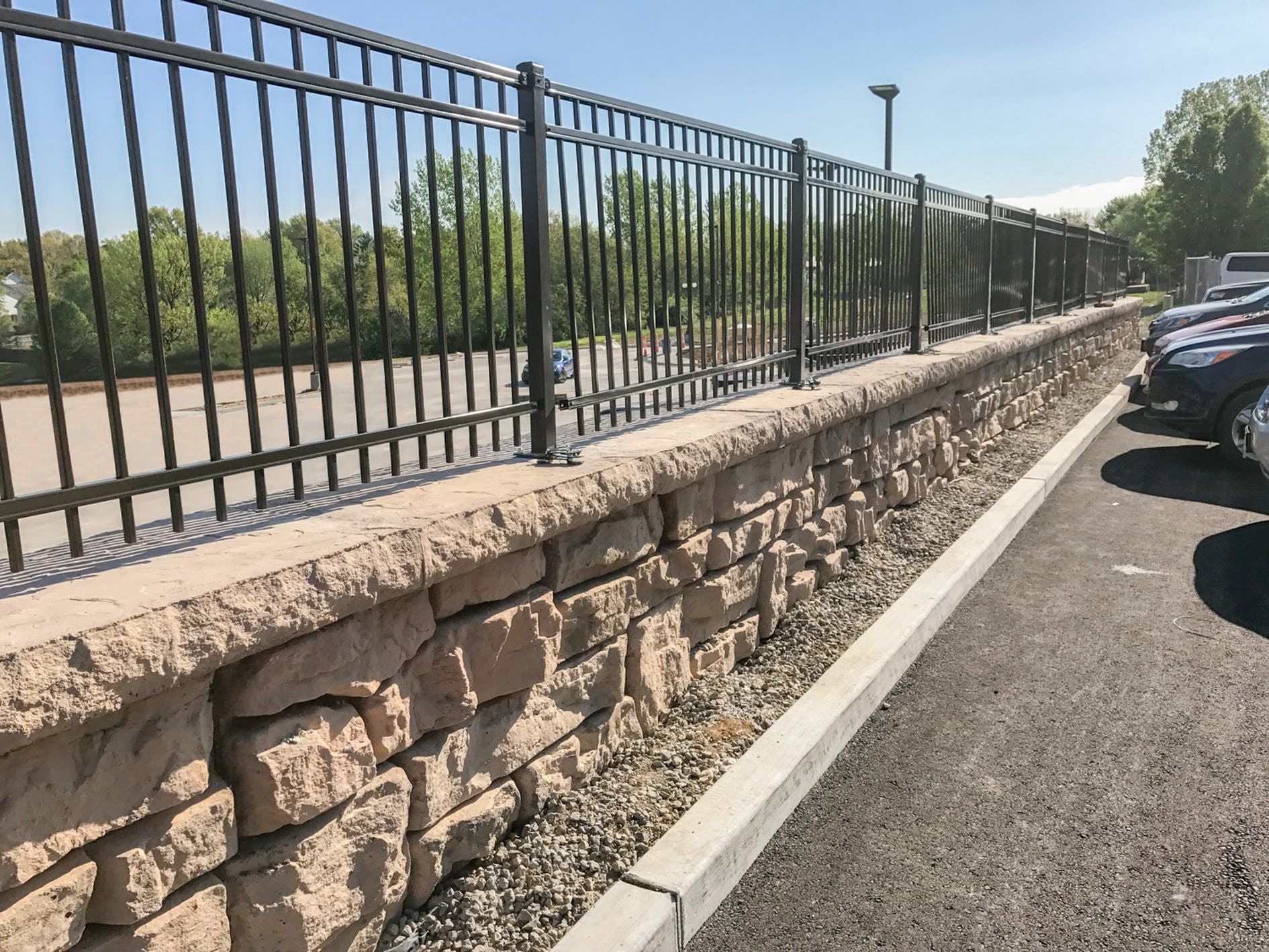 A parking lot with a stone wall and a metal fence
