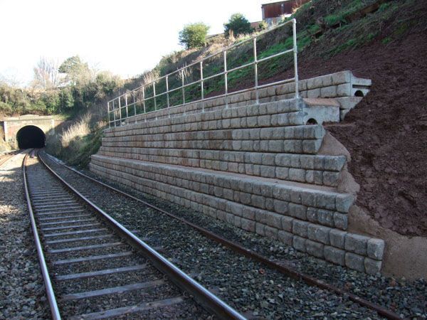 A train track with a retaining wall and a tunnel in the background