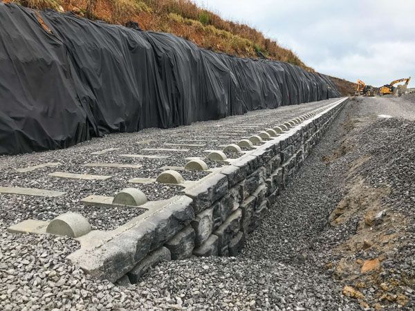 A train track is being built next to a stone wall.