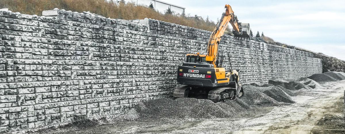 A yellow excavator is working on a brick wall.