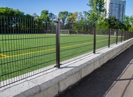 A fence surrounds a soccer field in a park.