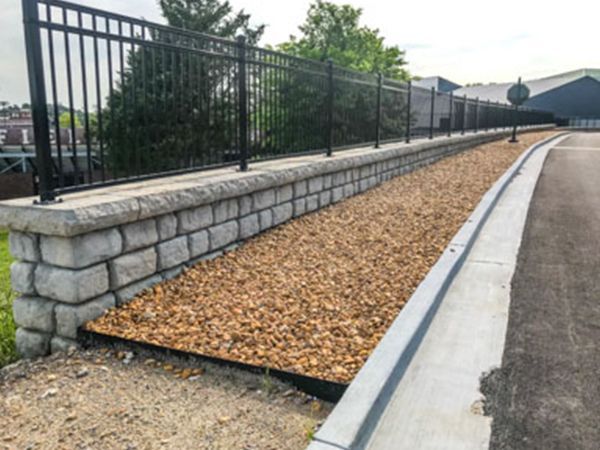 A brick wall along the side of a road next to a fence