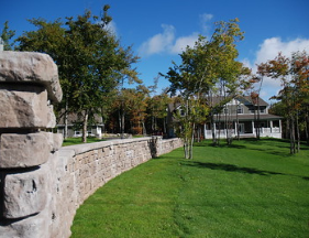 A stone wall surrounds a lush green field with a house in the background