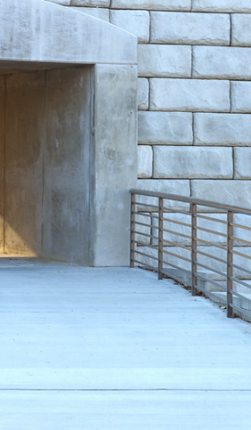A concrete ramp leading to a brick wall with a railing.