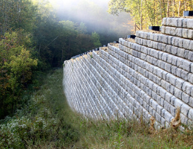A large stone wall is surrounded by trees and grass on a hillside.