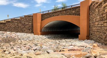 A tunnel under a bridge with a brick wall surrounding it.