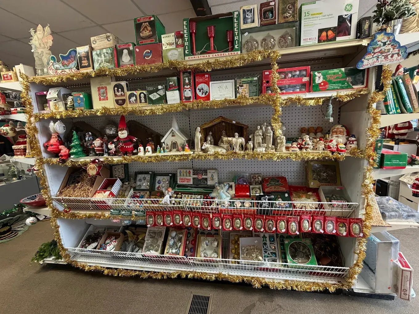 Shelves overflowing with Christmas decorations; various figurines, ornaments, and tinsel in a store.