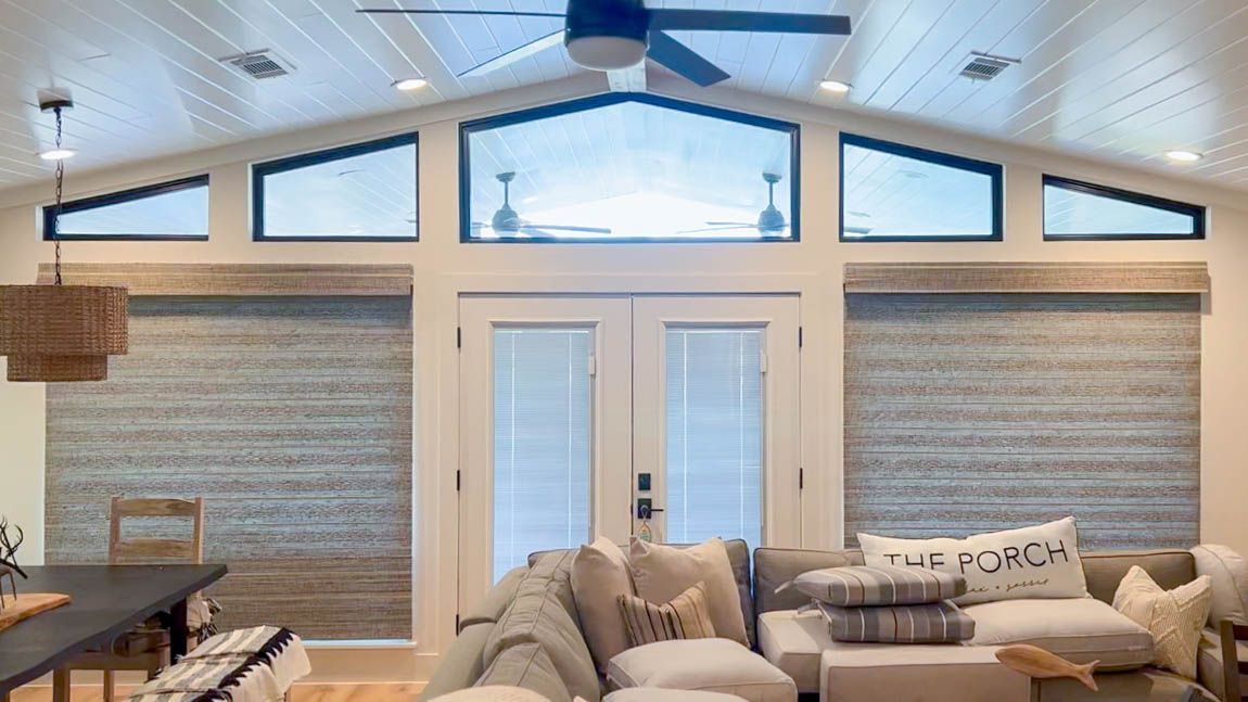 Bright living room with vaulted ceiling, triangular windows, and a beige sofa facing a stone fireplace with Roller Shades.