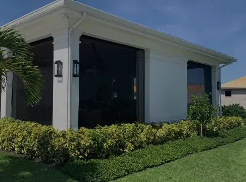 Modern white house with large dark windows, manicured hedges, and green lawn under a clear blue sky