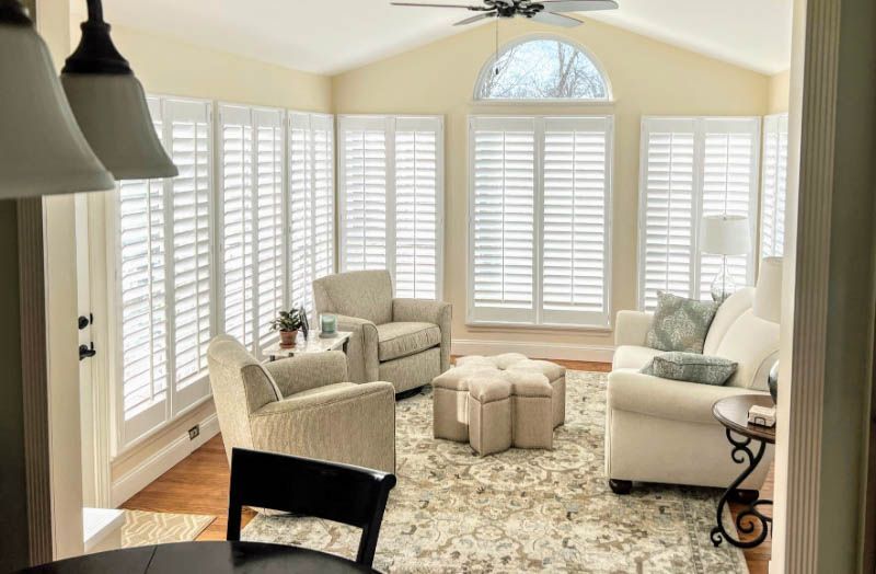 A living room full of windows has white shutters and an arched window. 