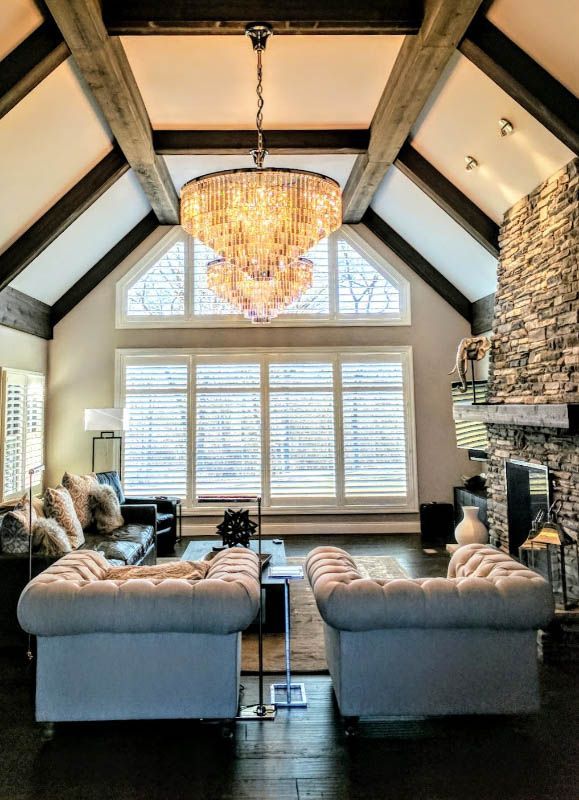 A living room with a chandelier has large, unique windows with shutters. 