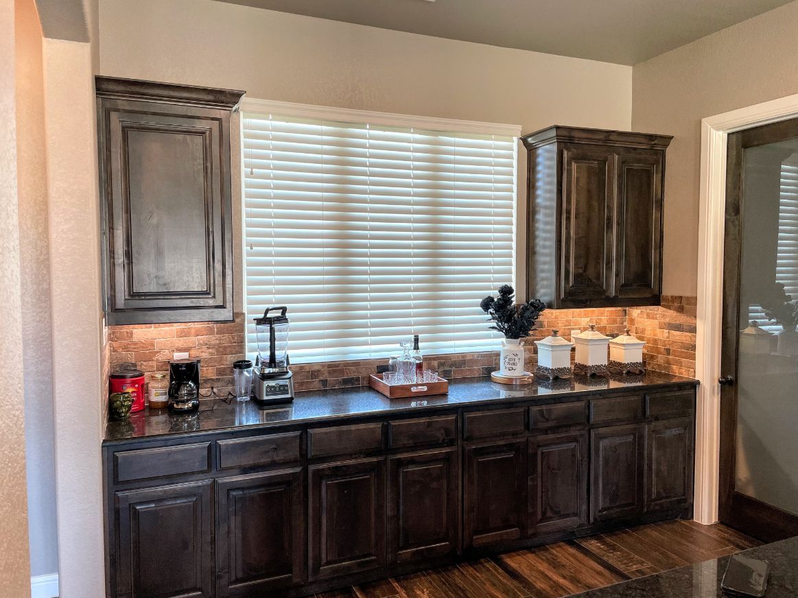 Kitchen with dark cabinets, countertop, and window with blinds.