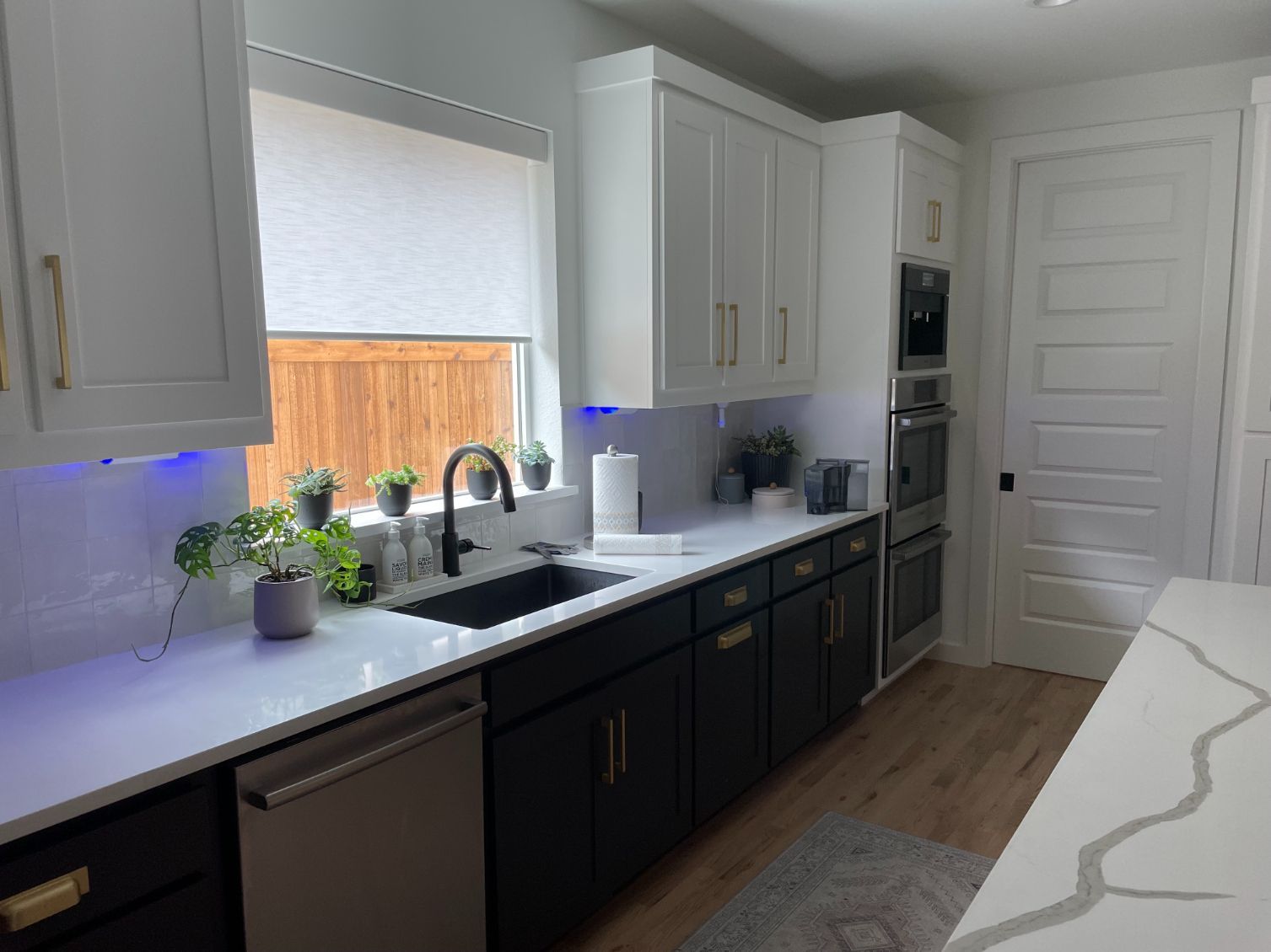 Modern kitchen with white upper cabinets, black lower cabinets, stainless steel appliances, and a window over the sink.
