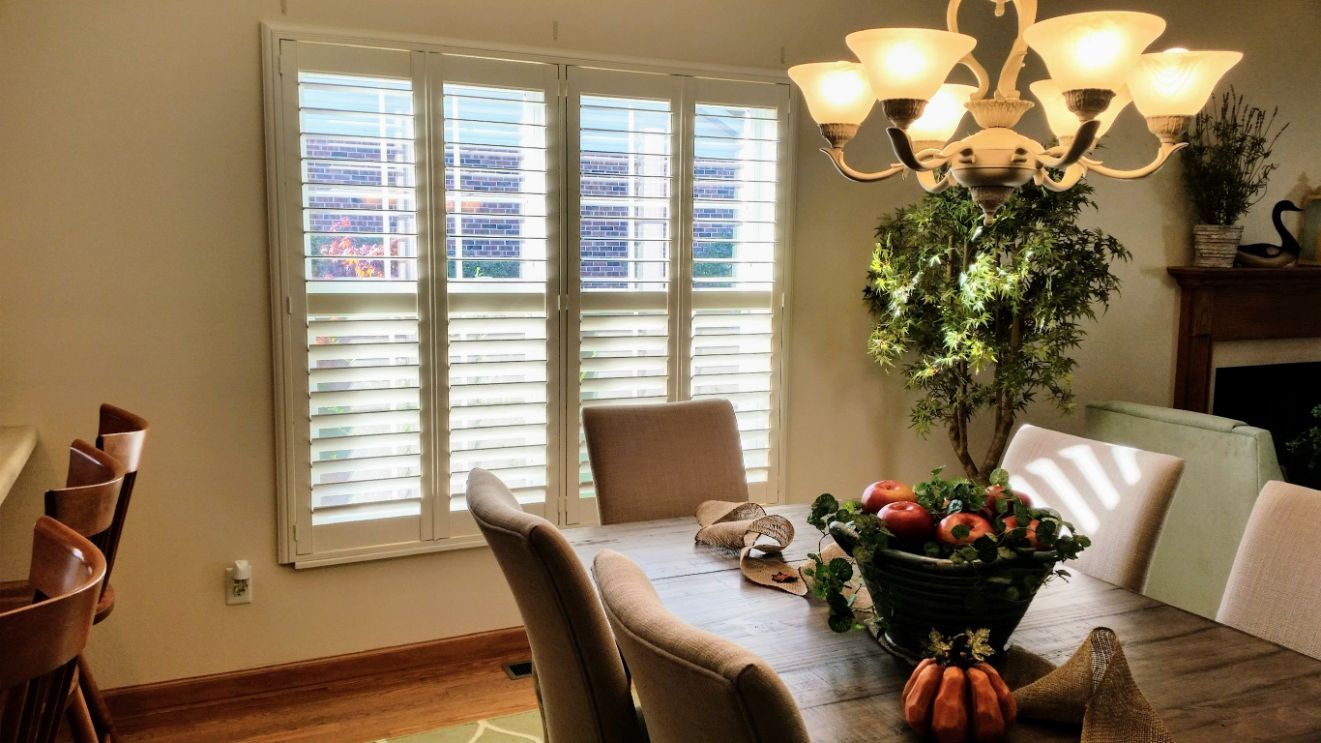 Dining room with shutters on a window, a wooden table with chairs, and a chandelier.
