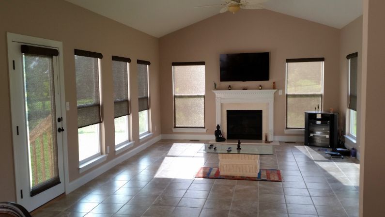 Love is Blinds TX: A living room with a fireplace and a flat screen tv and many windows with roller shades. 