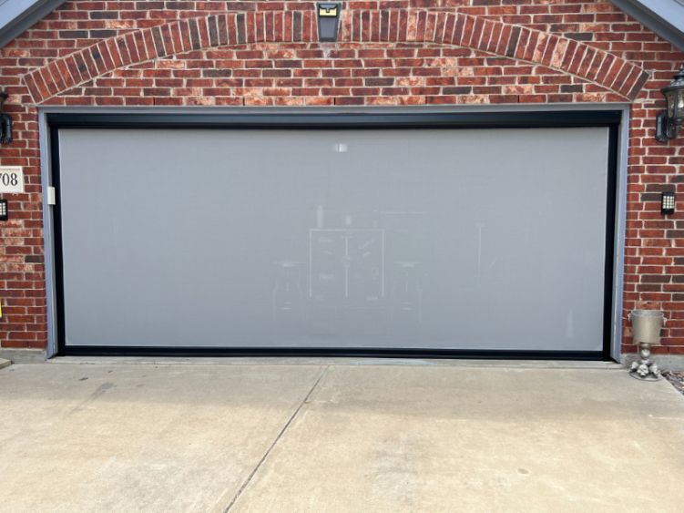 A red brick home has a garage with white exterior patio shades. 