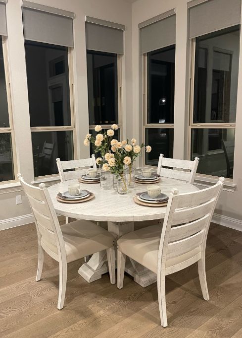 A dining room table and chairs with a vase of flowers on it and windows with cordless window treatments. Love is Blinds