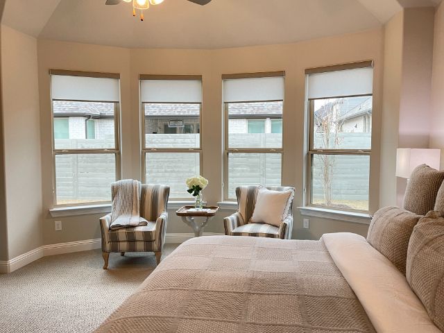 A bedroom with a large bed and two chairs, with cordless window shades on bay window. 