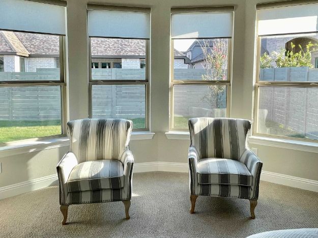 A sitting area with two chars has a bay window with roller shades. 