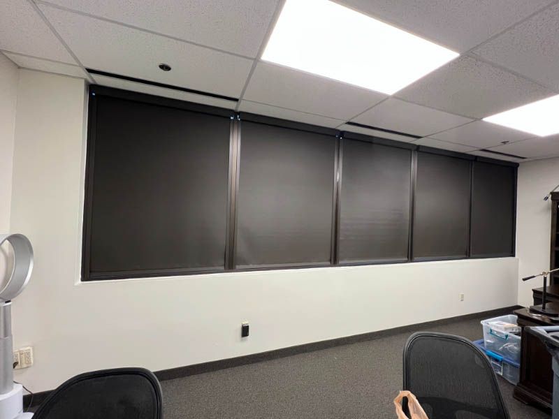 Love is Blinds TX: An office workroom with windows with black roller blinds on them.