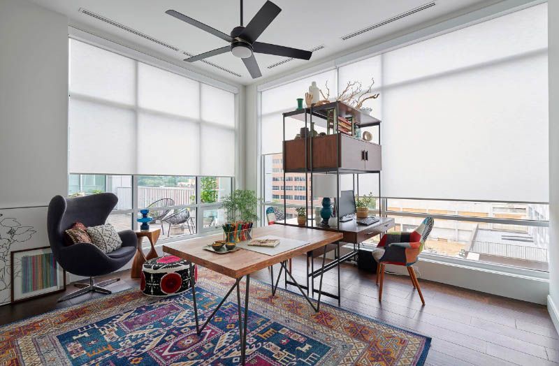 Love is Blinds TX: Roller shades in a corner office with a desk, chairs and a ceiling fan.