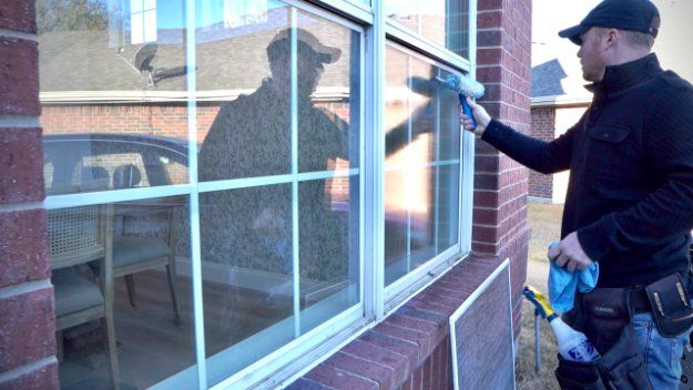 a man is cleaning a window on a brick building quarterly window washing services Love is Blinds.