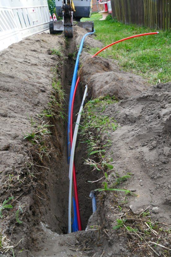 Trench With Blue, Red, And White Pipes Being Installed — Aliance Group in Macksville, NSW