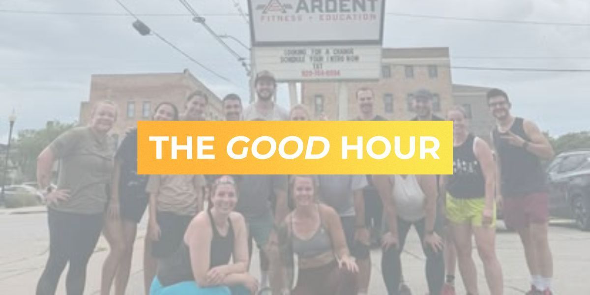 Group posing outdoors with a yellow banner reading “THE GOOD HOUR” in front of a building