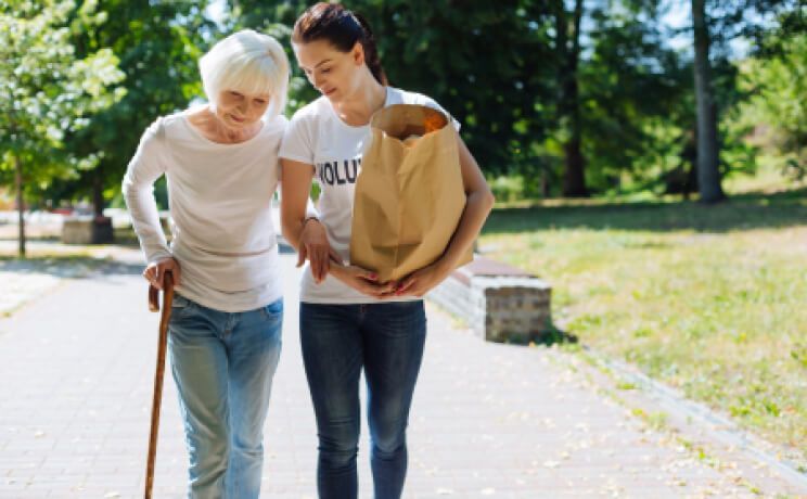 A young woman is helping an older woman walk down a sidewalk.