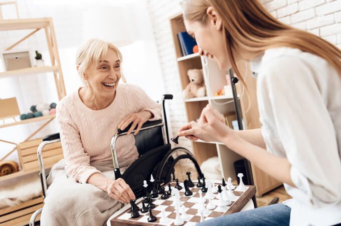 An elderly woman in a wheelchair is playing chess with a young woman.