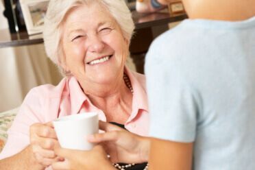 An elderly woman is smiling while holding a cup of coffee.