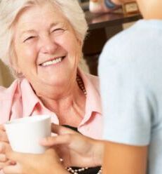 An elderly woman is smiling while holding a cup of coffee.