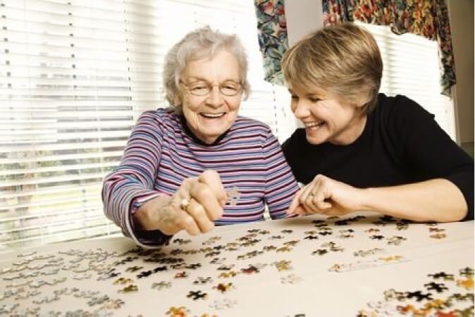 Two women are sitting at a table doing a puzzle together.